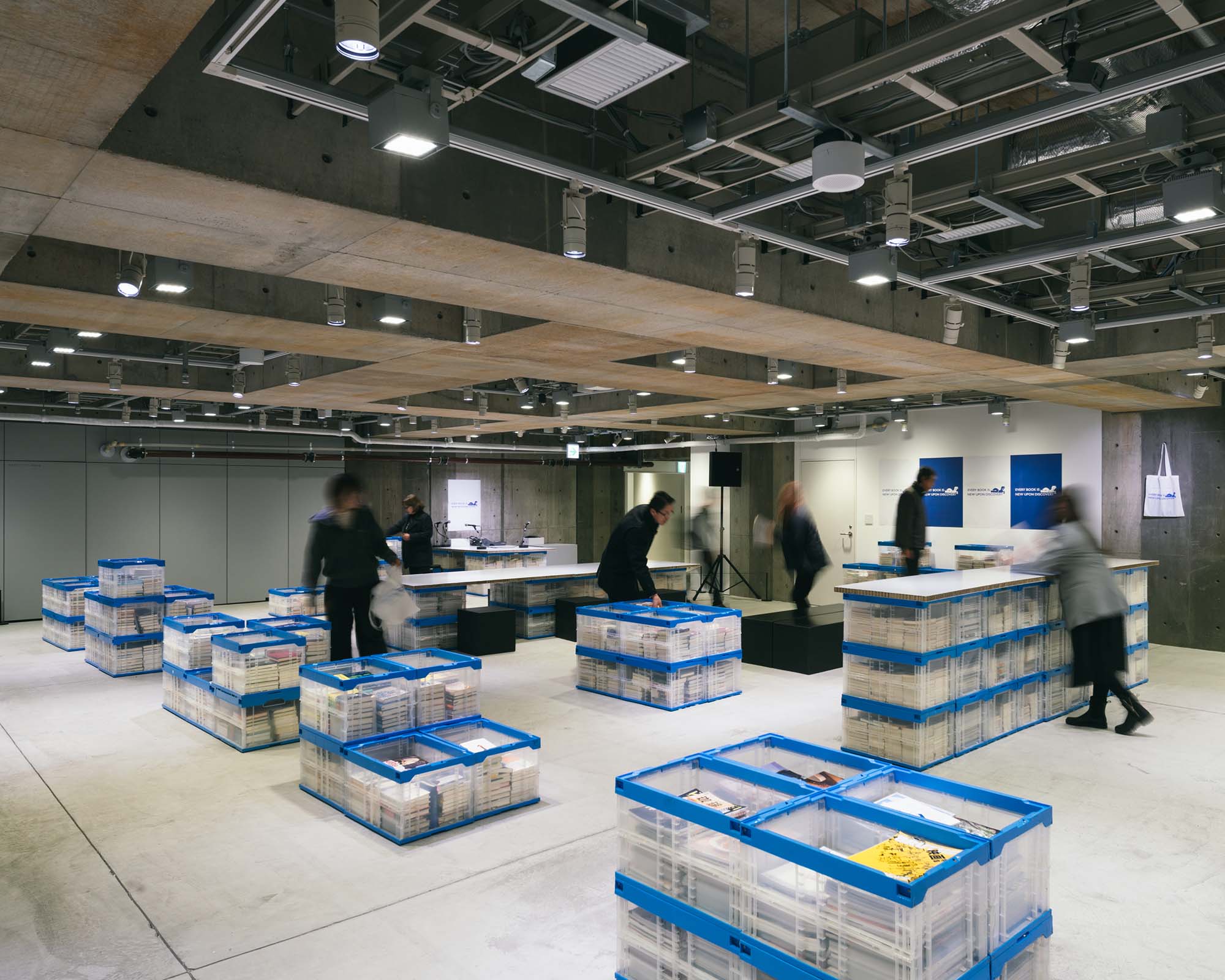 Inside Ginza Sony Park, books fill blue containers across the floor as visitors browse and move through the open exhibition space.