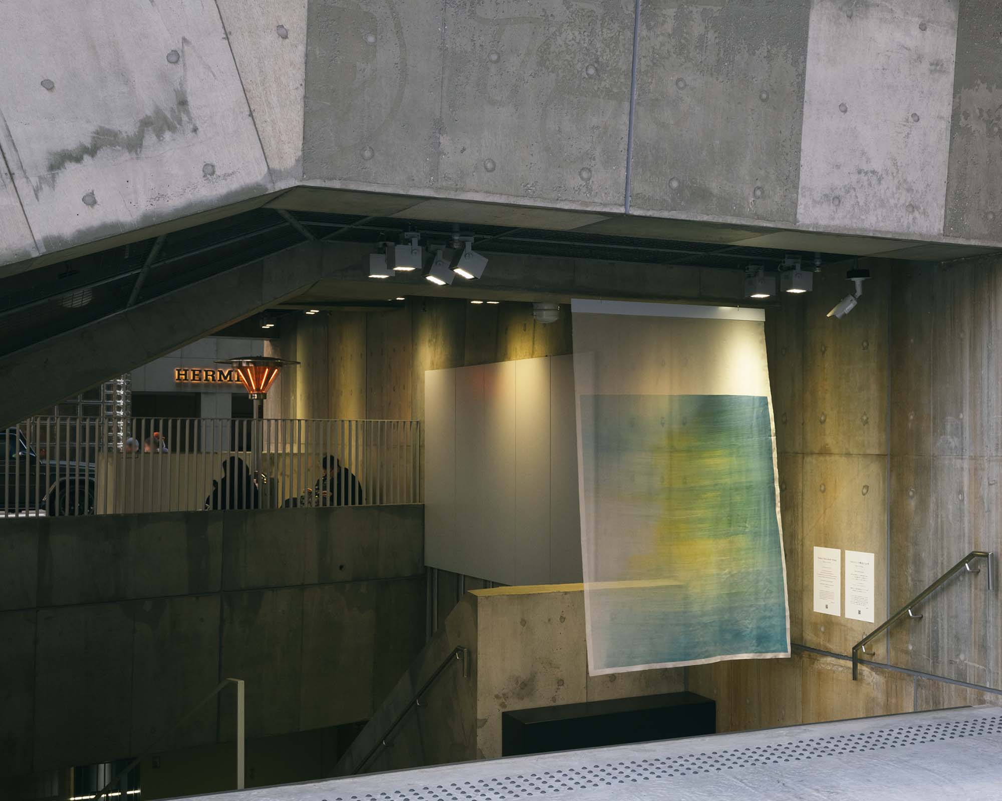 Beside a stairway at Ginza Sony Park, a translucent artwork hangs softly, its muted colors contrasting with the raw concrete walls.