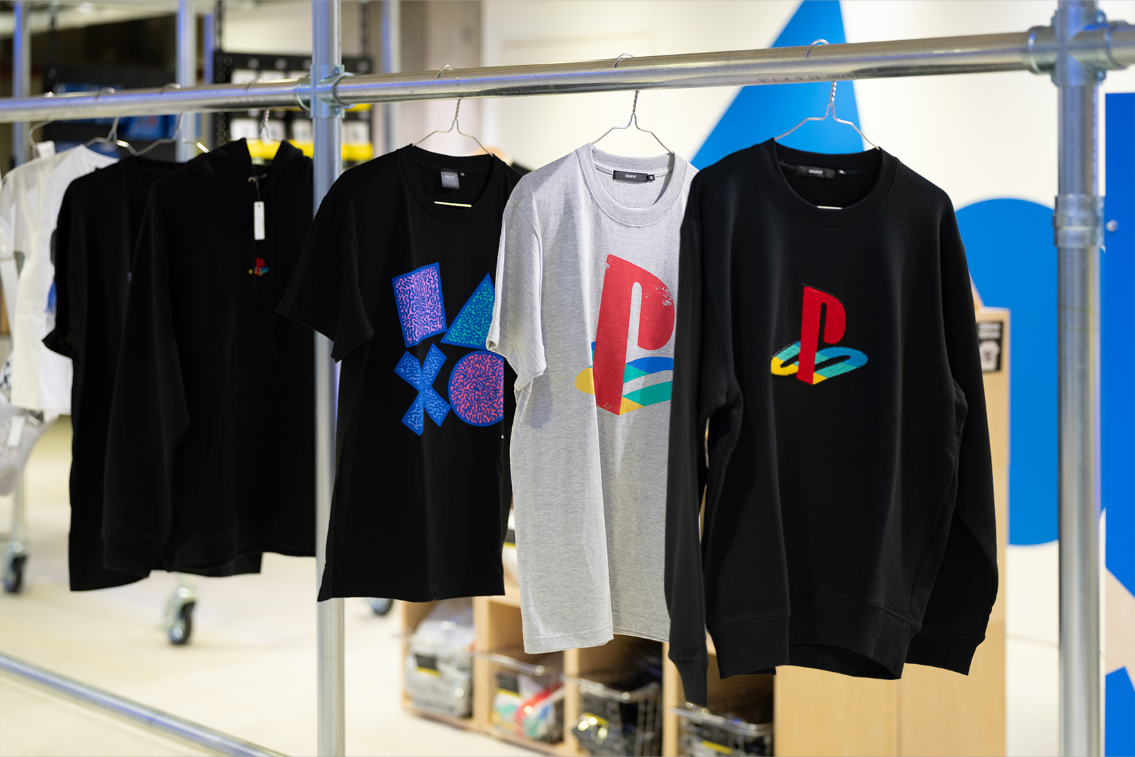 Photo of the B2 PlayStation merchandise shop, showcasing sweatshirts and T-shirts embroidered with the PlayStation logo, as well as T-shirts printed with motifs of ▲●✕■.